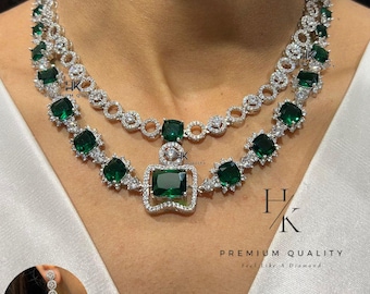 May include: A two-strand necklace with emerald-cut green gemstones and clear stones. The necklace has a square pendant with a large green gemstone. A matching earring is shown in a circular inset. The text "PREMIUM QUALITY feel like a Diamond" is visible.