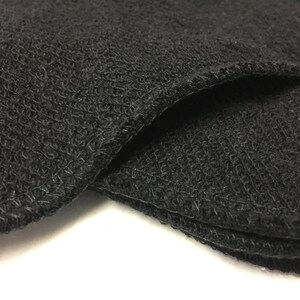 May include: Close-up of several black, round, textured fabric pads. The pads have a woven appearance and are stacked, with the edges showing a neat, stitched finish. The fabric appears soft and slightly fuzzy.