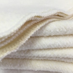 May include: A stack of white, soft, and fluffy fabric squares. The fabric is folded neatly and has a slightly textured surface.