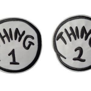 Könnte beinhalten: Zwei runde Aufnäher mit den schwarzen Schriftzügen „THING 1“ und „THING 2“ über den Zahlen 1 und 2. Text und Zahlen befinden sich auf weißem Grund, umrandet von einem schwarzen Rand. Die Aufnäher sind für Kleidung oder Accessoires gedacht.