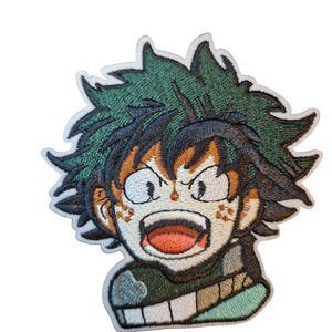 Puede incluir: Parche bordado con un personaje de dibujos animados con pelo verde puntiagudo, detalles en naranja y boca abierta. El personaje tiene una expresión decidida y está delineado en negro. Sobre fondo blanco.