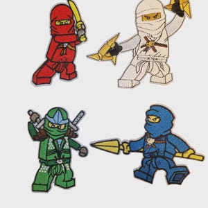Pode incluir: Quatro patches bordados com personagens ninja em vermelho, branco, verde e azul. Cada ninja segura uma arma, como uma espada ou lança. Os patches são projetados com uma estética de desenho animado.