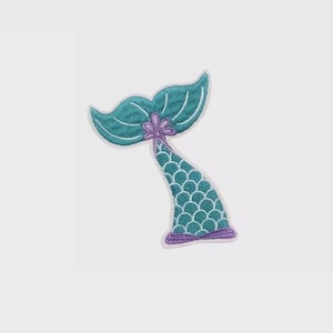 Op de afbeelding: Geborduurde zeemeerminstaart patch in tinten van teal, paars en wit. De staart heeft een schubbenpatroon en een bloemdetail aan de basis van de staartvin. De patch is ontworpen om op stof te strijken of te naaien.