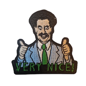 May include: Embroidered patch featuring a smiling man in a blue suit, green tie, and white shirt, giving two thumbs up. The text "VERY NICE!" is displayed in green below the figure, on a black background.