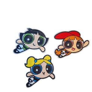 May include: Three embroidered patches featuring the Powerpuff Girls cartoon characters. Buttercup has black hair and a green outfit. Blossom has orange hair and a red bow. Bubbles has blonde hair and a blue outfit.