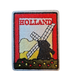 May include: Embroidered patch with a Dutch windmill design and the word "HOLLAND". The patch has a red border, a white background, and a landscape in yellow and green. The patch is rectangular.