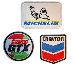 May include: Three embroidered patches featuring automotive brand logos. One rectangular patch displays the Michelin mascot and text. One circular patch features the Castrol GTX Motor Oil logo in red, green, and black. One shield-shaped patch shows the Chevron logo.
