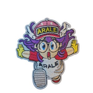 Puede incluir: Parche bordado con un personaje de dibujos animados con pelo morado, ojos azules grandes y guantes amarillos. El personaje lleva una camisa blanca y una gorra rosa con la palabra "ARALE". Fondo blanco.