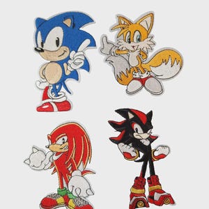 Può includere: Un set di quattro toppe ricamate raffiguranti personaggi di Sonic the Hedgehog. La collezione include un Sonic blu, un Tails giallo e bianco, un Knuckles rosso e uno Shadow nero e rosso, ognuno in una posa distinta con filo dai colori vivaci.