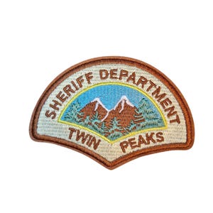 Op de afbeelding: Geborduurde patch met de woorden "SHERIFF DEPARTMENT" en "TWIN PEAKS" in een halfrond ontwerp. De patch bevat een berglandschap met een blauwe lucht en groene bomen, omlijst door een bruine rand.