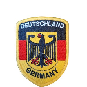 Könnte beinhalten: Gestickter Aufnäher mit dem deutschen Wappen. Der Aufnäher hat einen gelben Rand und eine Schildform. Oben auf dem Aufnäher steht "DEUTSCHLAND" und unten "GERMANY". Der Schild zeigt einen schwarzen Adler mit roten Akzenten und die Farben der deutschen Flagge.