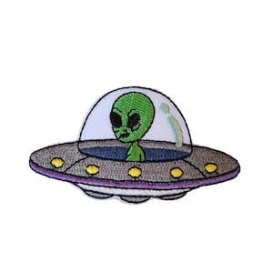 Può includere: Toppa ricamata raffigurante un alieno verde in un UFO. L'UFO è grigio con dettagli gialli e viola, e l'alieno ha grandi occhi neri. La toppa è progettata per essere stirata o cucita sul tessuto.