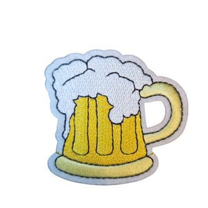 May include: Embroidered patch depicting a yellow beer mug with white foam. The mug has a curved handle and a light yellow outline. The foam is detailed with white stitching, and the mug is filled with yellow liquid.