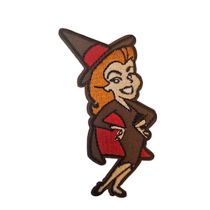 Könnte beinhalten: Gestickter Aufnäher mit einer Cartoon-Hexe mit orangefarbenem Haar, die ein braunes Kleid, einen roten Umhang und einen spitzen Hut mit rotem Band trägt. Die Hexe lächelt und hat die Hände in den Hüften.
