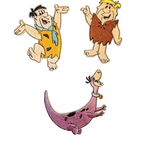 Może przedstawiać: Haftowane naszywki przedstawiające postacie z kreskówek Freda Flinstone'a, Barneya Rubble'a i Dino. Fred ma na sobie pomarańczową tunikę i niebieski krawat. Barney ma brązową tunikę. Dino to fioletowy dinozaur z czarnymi plamami i obrożą.