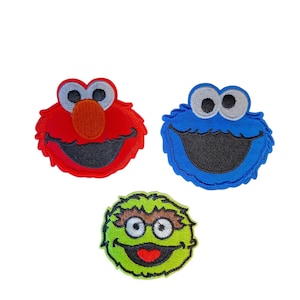 May include: Three embroidered patches featuring the faces of popular children's television characters. One patch is red with a large orange nose, one is blue with a wide mouth, and one is lime green with brown eyebrows and a red heart-shaped mouth.