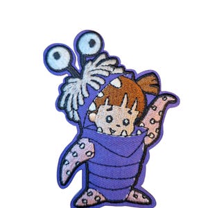 May include: Embroidered patch featuring a cartoon character from the movie Monsters, Inc. The patch depicts Boo in a purple monster costume with large eyes and tentacles. The patch is outlined in a dark purple.