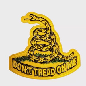 Op de afbeelding: Geborduurde patch met een opgerolde gele ratelslang op een gele achtergrond. De patch bevat de tekst "DON'T TREAD ON ME" in zwart, met groen gras aan de onderkant. De patch heeft een gele rand.