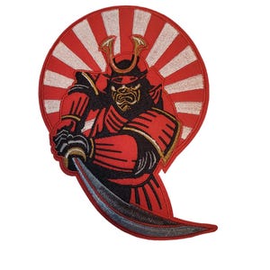 Könnte beinhalten: Gestickter Aufnäher mit einem Samurai-Krieger in roter und schwarzer Rüstung, der ein Katana hält. Der Samurai ist vor einem rot-weißen Sonnenaufgangsdesign mit goldenen Akzenten auf Helm und Rüstung platziert.