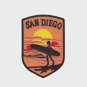 May include: Embroidered patch featuring a sunset scene with a surfer and surfboard. The patch is orange with a yellow sun, red clouds, and the text "SAN DIEGO" in black.