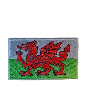Può includere: Toppa ricamata con la bandiera gallese. Il design presenta un drago rosso su sfondo grigio, con una striscia verde nella parte inferiore. La toppa è rettangolare e ha un bordo cucito.