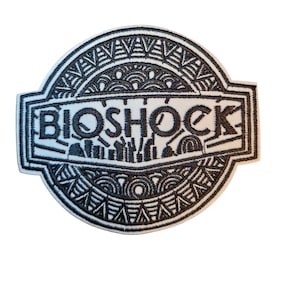 Könnte beinhalten: Gestickter Aufnäher mit dem Wort "BIOSHOCK" in Schwarz auf weißem Hintergrund. Der Aufnäher hat ein kreisförmiges Design mit komplizierten schwarzen Mustern und einer rechteckigen Bannerform. Geeignet für Kleidung oder Accessoires.