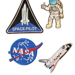 May include: Four embroidered space-themed patches. Features include a triangular patch with a shuttle and "SPACE PILOT" text, a NASA logo, an astronaut giving a thumbs up, and a shuttle.