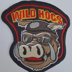 Peut inclure: Écusson brodé représentant un sanglier de dessin animé portant un casque d'aviateur en cuir et des lunettes de soleil. L'écusson porte l'inscription "WILD HOGS" en lettres jaunes et rouges. L'écusson est bordé d'un motif rouge et noir.