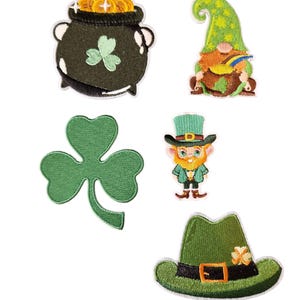 May include: A collection of embroidered patches featuring St. Patrick's Day themes. Includes a pot of gold, a green gnome, a green shamrock, a leprechaun, and a green hat with a buckle and shamrock detail. All patches have white borders.