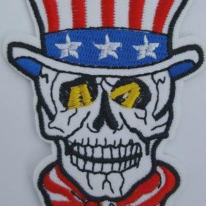 May include: Embroidered patch featuring a skull wearing a patriotic Uncle Sam hat with red and white stripes and a blue band with white stars. The skull has yellow eyes and a red and white striped bow tie.