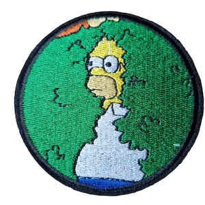 Op de afbeelding: Ronde geborduurde patch met Homer Simpson voor een groen wereldbolontwerp. De patch heeft een zwarte rand en details in geel, wit, blauw en oranje. Een kleurrijk accessoire.