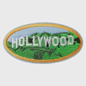 May include: An embroidered patch with the word "HOLLYWOOD" in white block letters. The patch features a green landscape design with a light blue background and a gold border. The patch is oval-shaped.