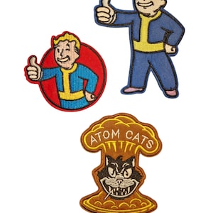 Op de afbeelding: Drie geborduurde patches met personages uit de Fallout-videogameserie. Twee patches tonen het Vault Boy-personage dat een duim omhoog geeft, één in een rode cirkel. De derde patch toont een zwarte kat met de tekst "ATOM CATS".