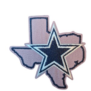 Puede incluir: Un parche de tela con el contorno del estado de Texas en color lila claro, con un contorno azul marino. Una estrella azul marino con un contorno blanco está centrada sobre el estado. El parche es probablemente para ropa o accesorios.