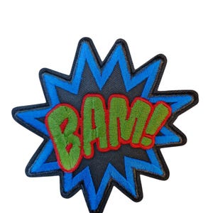 May include: A colorful patch with the word "BAM!" in green letters outlined in red. The text is set against a black background within a blue starburst shape, perfect for adding a comic book flair to clothing or accessories.