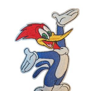 Op de afbeelding: Geborduurde patch met Woody Woodpecker in een dynamische pose. De patch toont het stripfiguur met een rode kop, gele snavel, blauw lichaam en witte handschoenen. Het ontwerp is gedetailleerd met geborduurde steken.