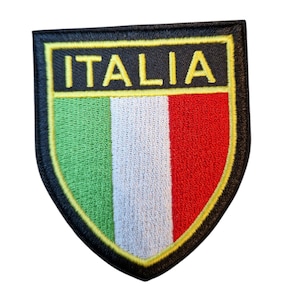 Könnte beinhalten: Gestickter Aufnäher in Schildform mit den vertikalen grünen, weißen und roten Streifen der italienischen Flagge. Das Wort "ITALIA" steht in Gelb auf schwarzem Grund über der Flagge. Der Aufnäher hat einen schwarzen Rand mit gelber Kontur.