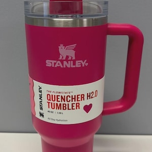 Pode incluir: Uma caneca de cer&acirc;mica branca com uma al&ccedil;a preta e o texto "But First, Coffee" em preto, com uma fonte manuscrita. A caneca est&aacute; sobre uma superf&iacute;cie branca.