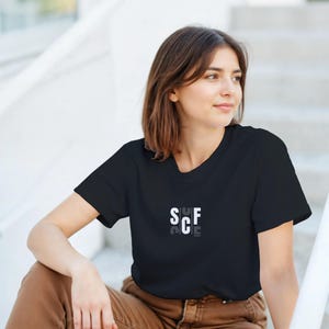 May include: Black crew neck t-shirt with the word "SCF" in a white, stylized font. The shirt is made of a soft material and is suitable for casual wear.