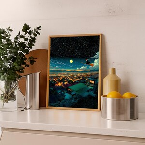 May include: A framed art print depicts a night scene with a witch flying on a broom over a city. The artwork features a starry sky, a full moon, and a vibrant cityscape with illuminated buildings. The frame is a light brown color.