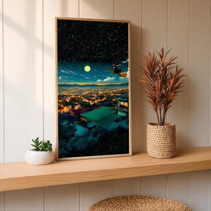 May include: A framed art print depicts a night scene with a witch flying on a broom over a city. The artwork features a starry sky, a full moon, and city lights. The print is displayed on a wooden shelf with a plant in a woven pot.