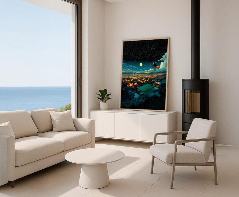 May include: A modern living room with a large framed art print depicting a nighttime cityscape with a full moon. The room features a beige sofa, a round coffee table, and a white cabinet. A black fireplace and a large window with a view of the ocean are also visible.