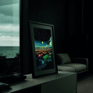 May include: A framed art print featuring a vibrant, colorful cityscape under a starry night sky. The artwork is displayed in a modern, dark-toned room, leaning against a wall. The print's colors contrast with the room's muted tones.