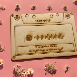 Könnte beinhalten: Ein Holz-Kassettenband-Design mit dem Datum 15.05.2023 und einem eingravierten Spotify-Code. Der Text "9 rocznica ślubu Wszystkiego Najlepszego!" ist ebenfalls eingraviert. Der Hintergrund ist rosa, mit kleinen weißen und gelben Blumen.