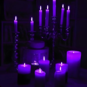 May include: A collection of lit purple candles in varying sizes and styles. Some are pillar candles, while others are taper candles in ornate candelabras. The scene is dimly lit, creating a dramatic and atmospheric effect.