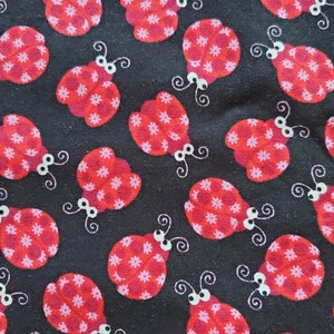 May include: A black fabric with a repeating pattern of red ladybugs with white polka dots. The ladybugs have white eyes and black antennae.
