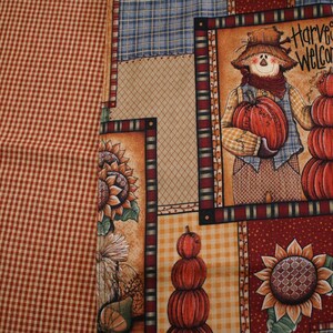 May include: A patchwork fabric with a fall harvest theme. The design includes a scarecrow holding a pumpkin, sunflowers, and stacked pumpkins. The fabric also features a red and white checkered pattern.
