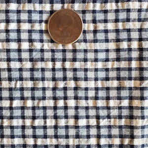 May include: A close-up of a white and blue gingham fabric with a US quarter on top. The quarter is a standard US coin with the words "United States of America" and "Liberty" visible.