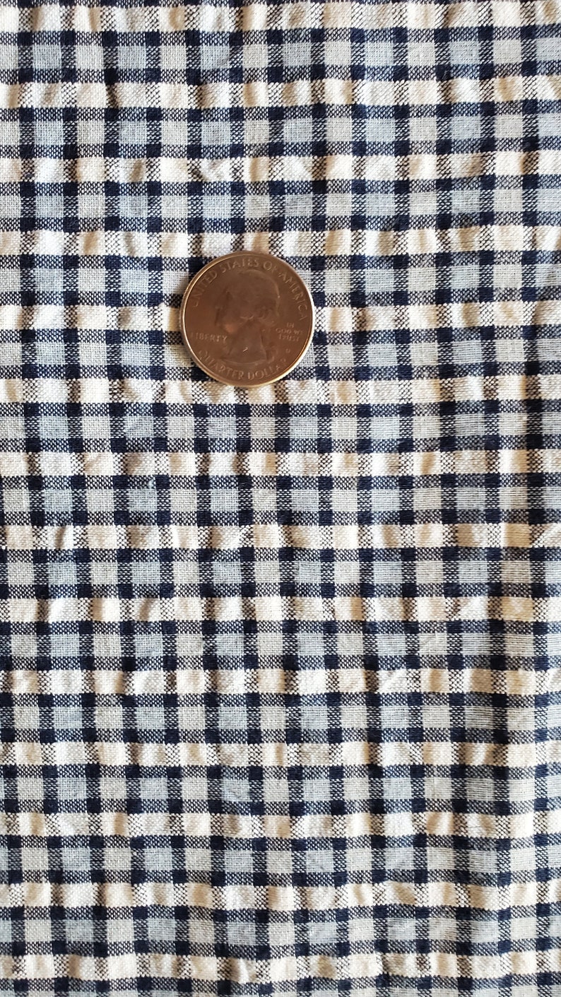 May include: A close-up of a white and blue gingham fabric with a US quarter on top. The quarter is a standard US coin with the words "United States of America" and "Liberty" visible.