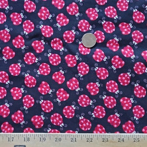 May include: Black fabric with a repeating pattern of red ladybugs. The ladybugs have white spots and are outlined in white.